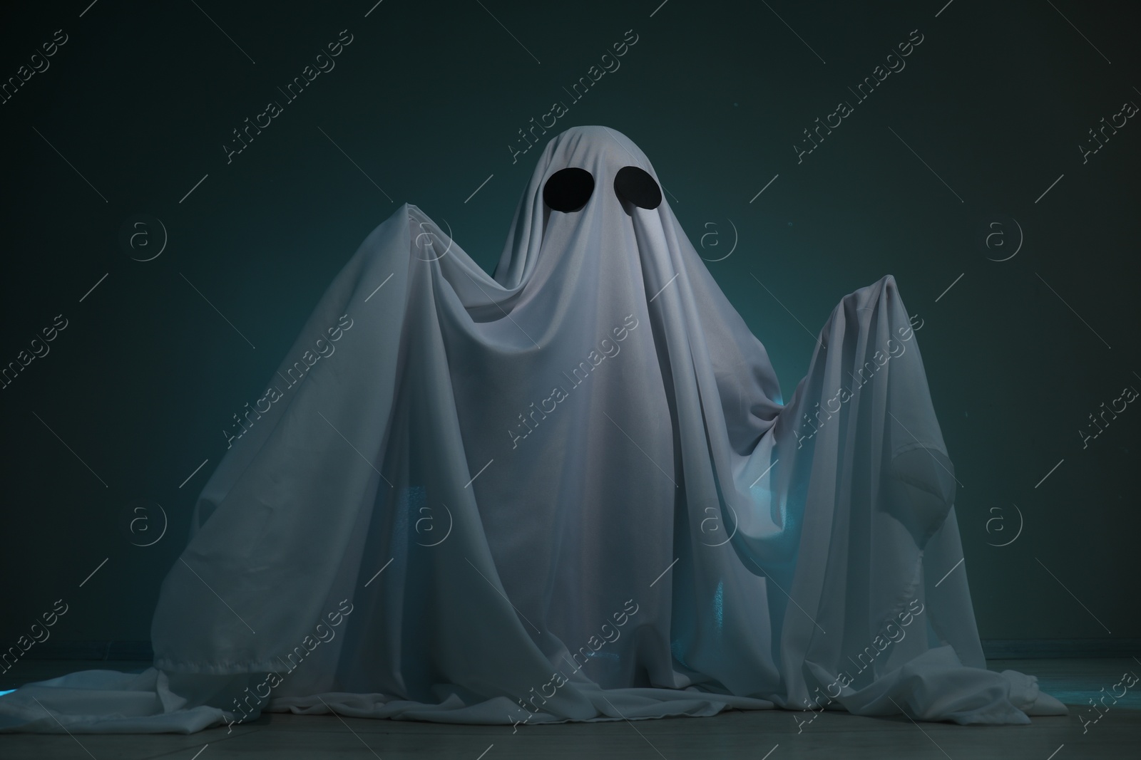 Photo of Creepy ghost. Woman covered with sheet on dark teal background