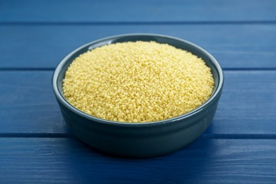 Bowl of raw couscous on blue wooden table, closeup
