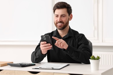 Photo of Smiling man using smartphone at table in office
