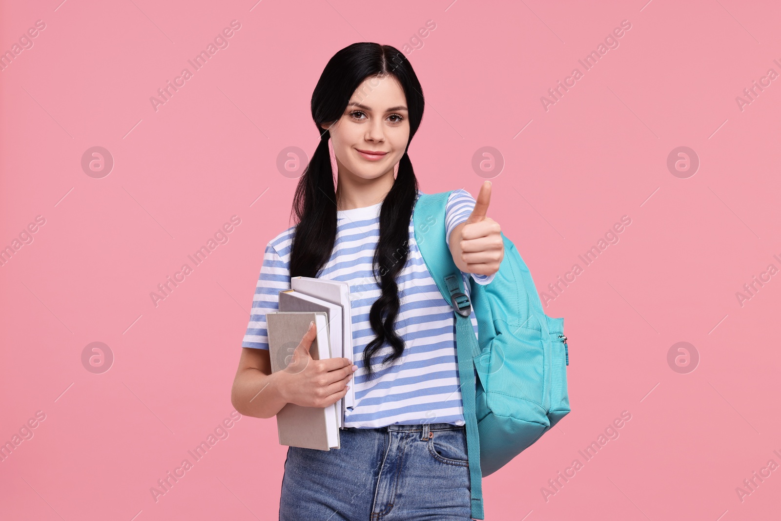 Photo of Student with books and backpack showing thumb up on pink background