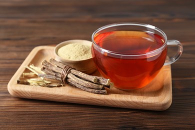 Photo of Aromatic licorice tea in cup, dried sticks of licorice root and powder on wooden table, closeup