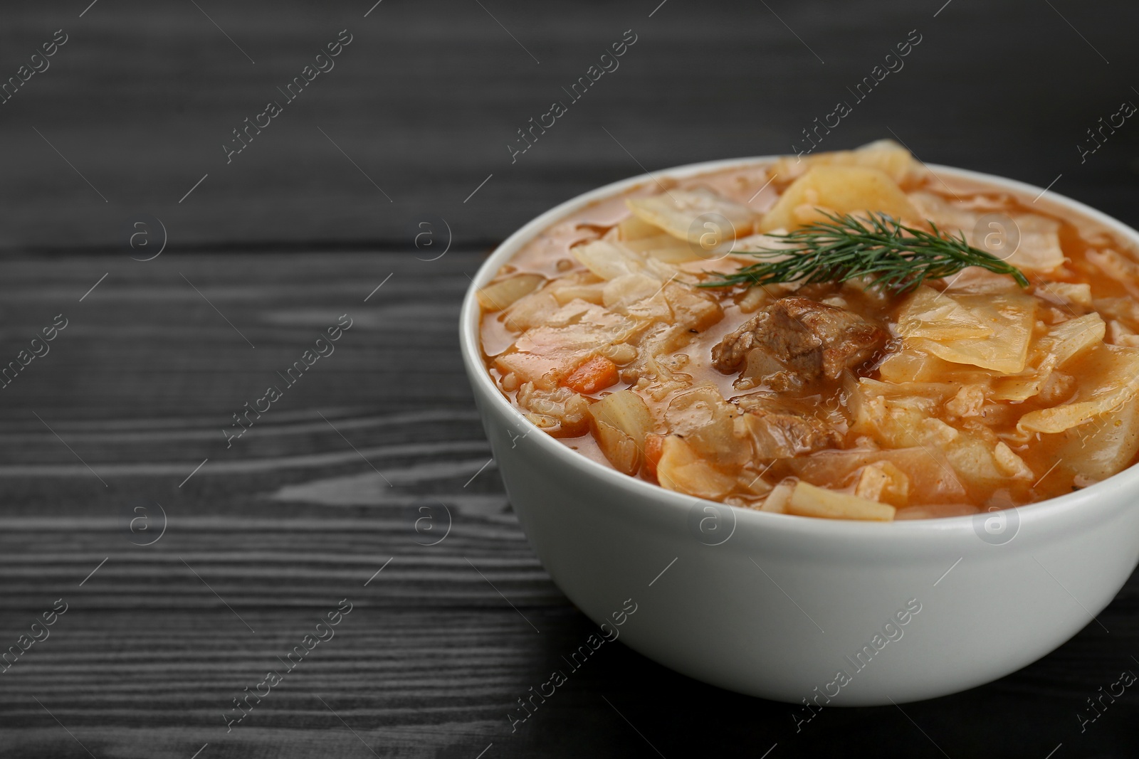 Photo of Tasty cabbage soup with meat, carrot and dill on black wooden table, closeup. Space for text