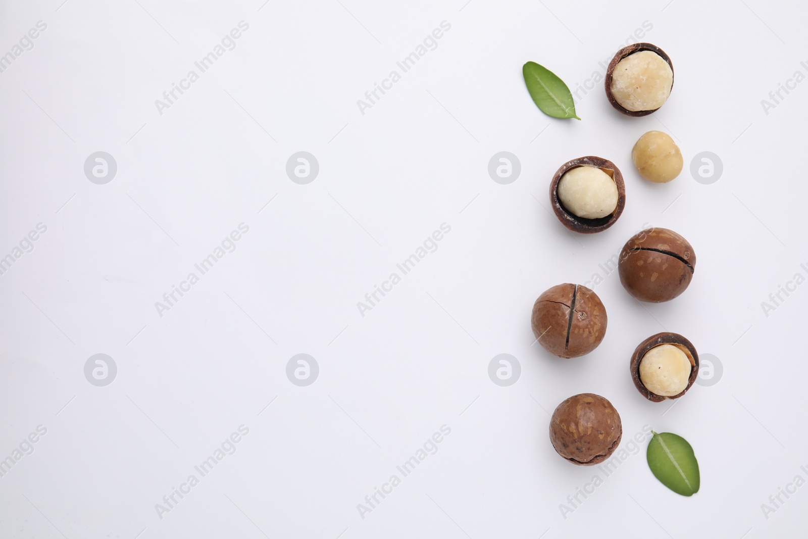 Photo of Tasty Macadamia nuts and green leaves on white background, flat lay. Space for text