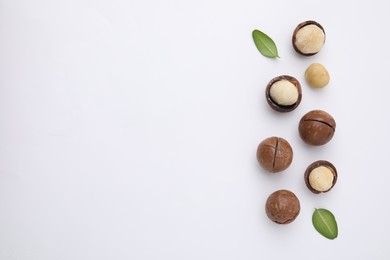 Tasty Macadamia nuts and green leaves on white background, flat lay. Space for text