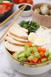 Delicious poke bowl with meat, egg, rice and vegetables served on white marble table, closeup