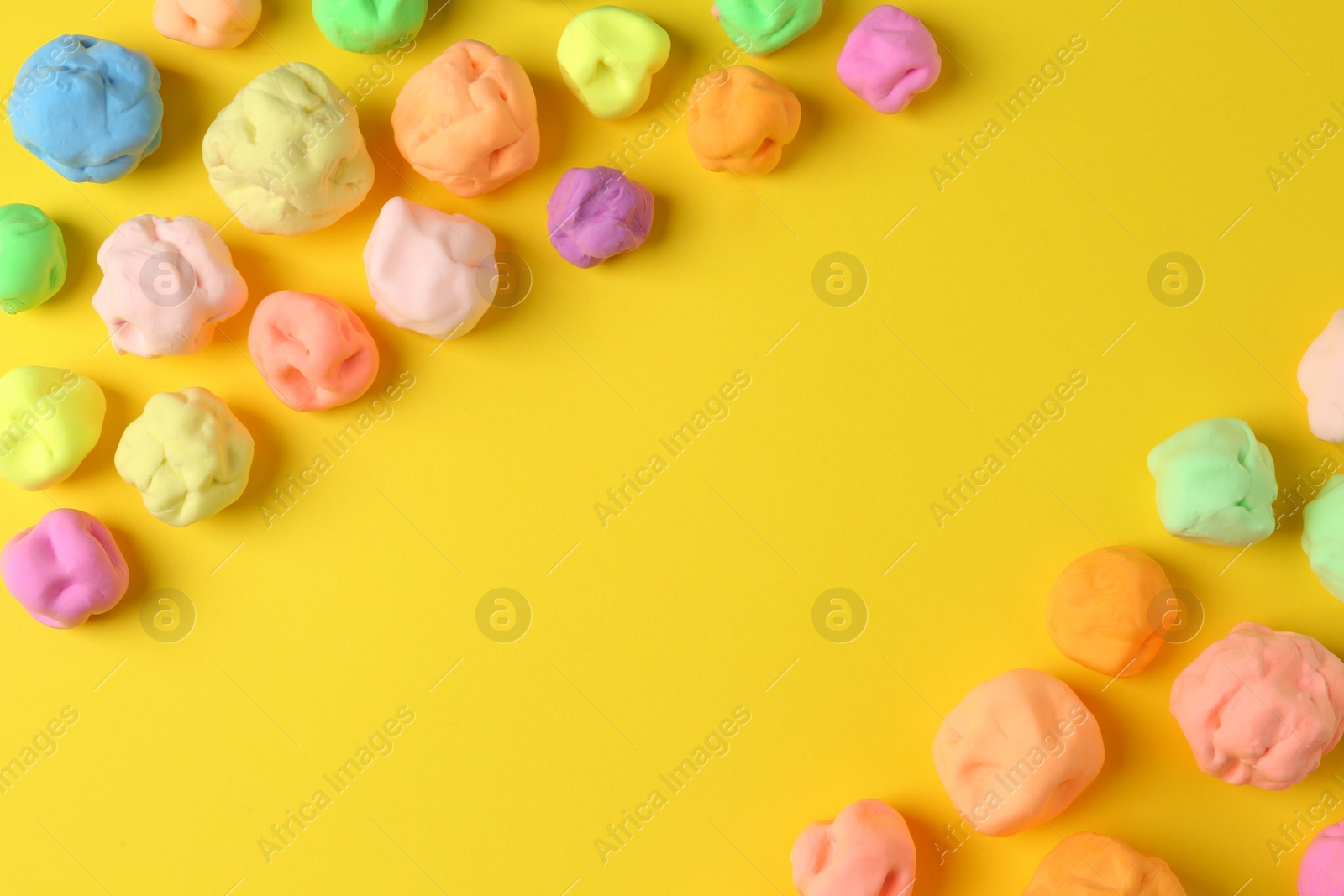 Photo of Different color play dough on yellow background, flat lay. Space for text