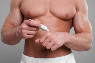 Photo of Man applying body cream onto his hand on light grey background, closeup