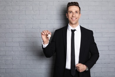 Male real estate agent with key on brick wall background