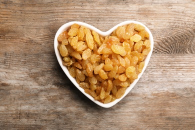 Photo of Heart shaped plate with raisins on wooden background, top view. Dried fruit as healthy snack