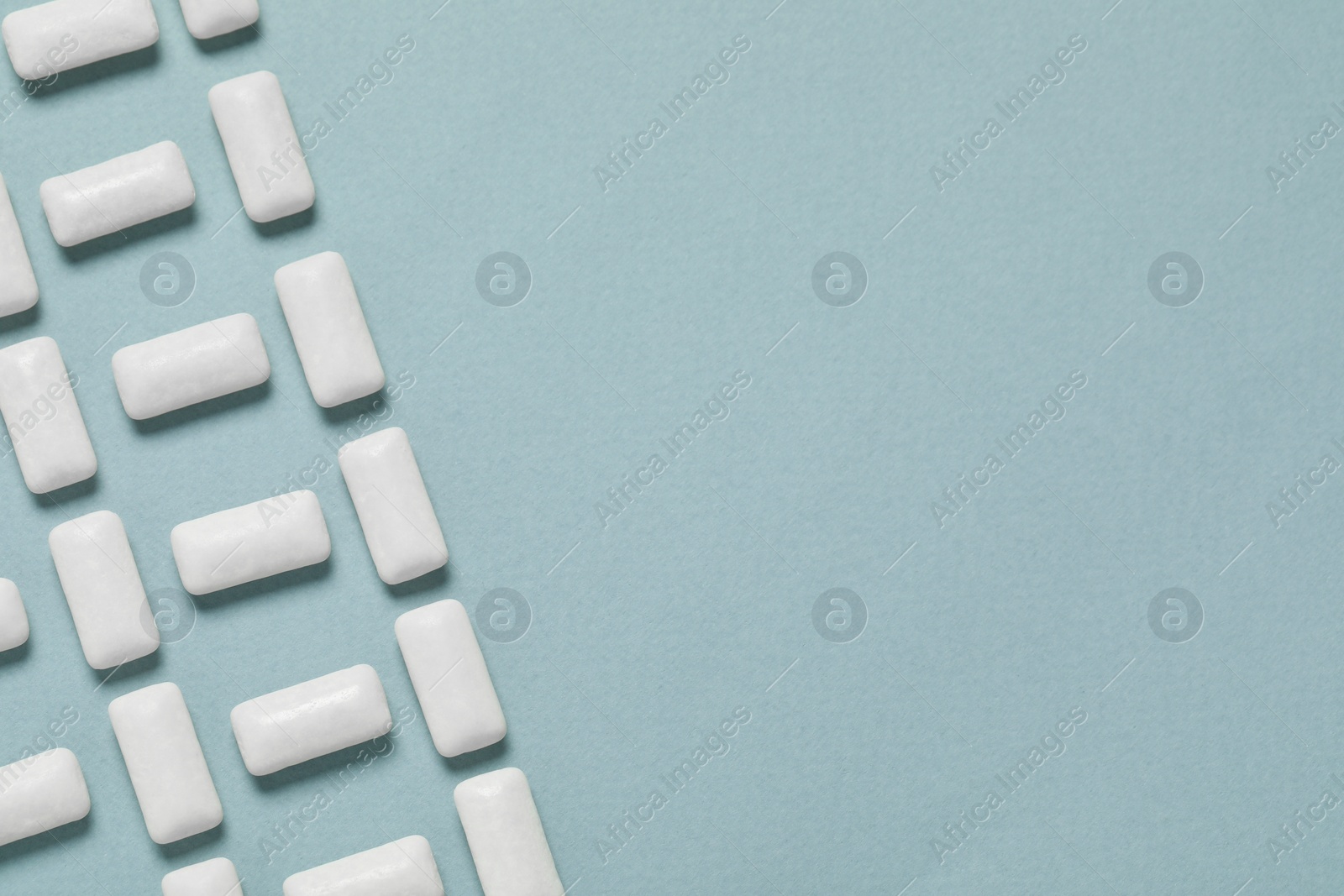 Photo of Tasty white chewing gums on light blue background, flat lay. Space for text