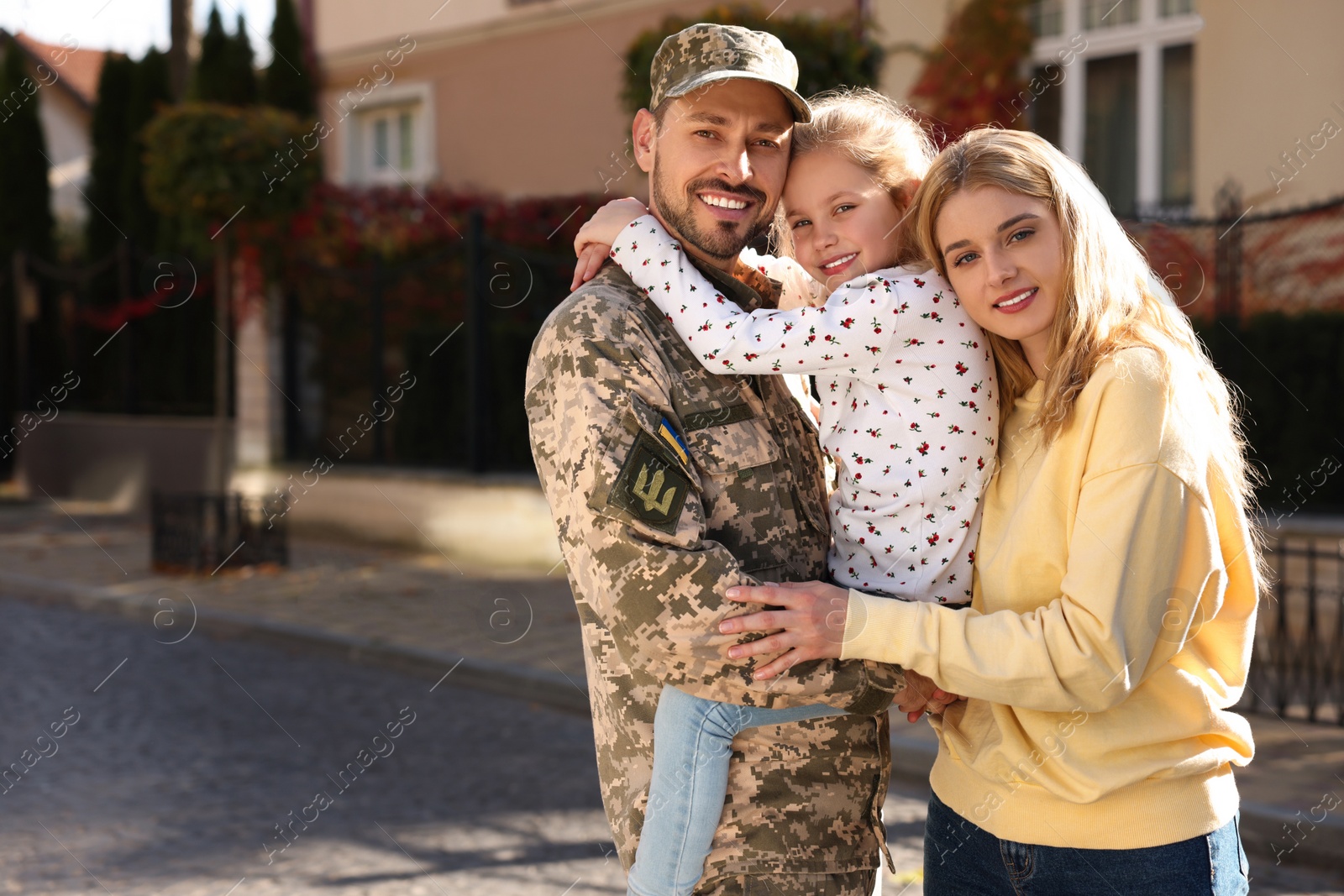 Photo of Soldier in Ukrainian military uniform reunited with his family on city street, space for text