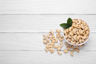 Tasty cashew nuts and green leaves on white wooden table, top view. Space for text