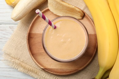 Glass of tasty banana smoothie with straw and fresh fruits on white wooden table, flat lay