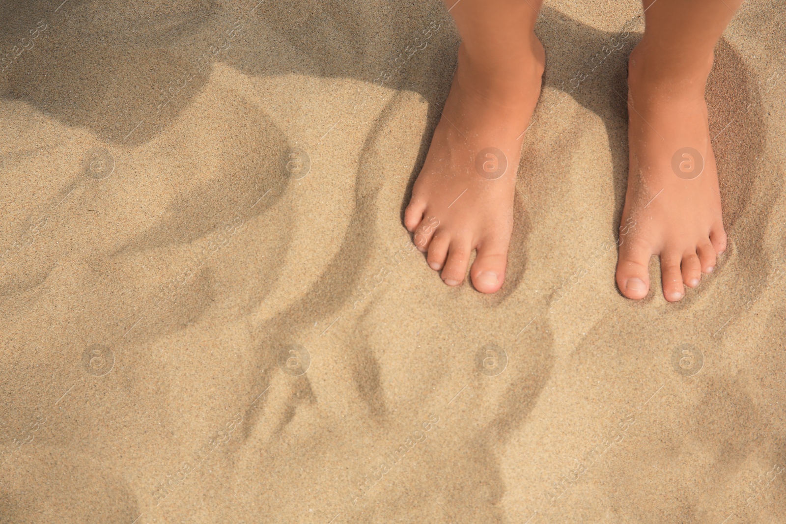 Photo of Little girl standing on sandy beach, closeup. Space for text