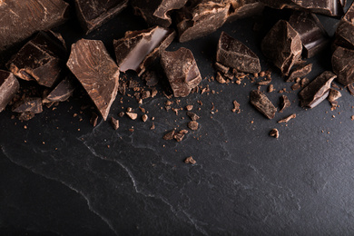 Photo of Pieces of dark chocolate on black table, flat lay