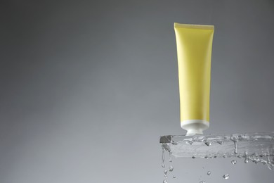 Photo of Moisturizing cream in tube on glass with water drops against grey background, low angle view. Space for text