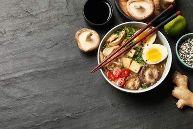 Photo of Noodle soup. Bowl of delicious ramen, ingredients and chopsticks on black table, flat lay. Space for text