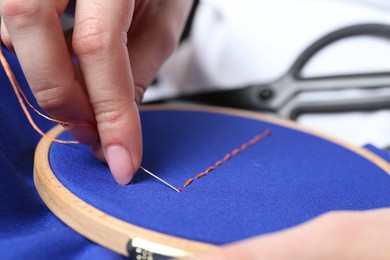 Photo of Woman with sewing needle and thread embroidering on cloth, closeup