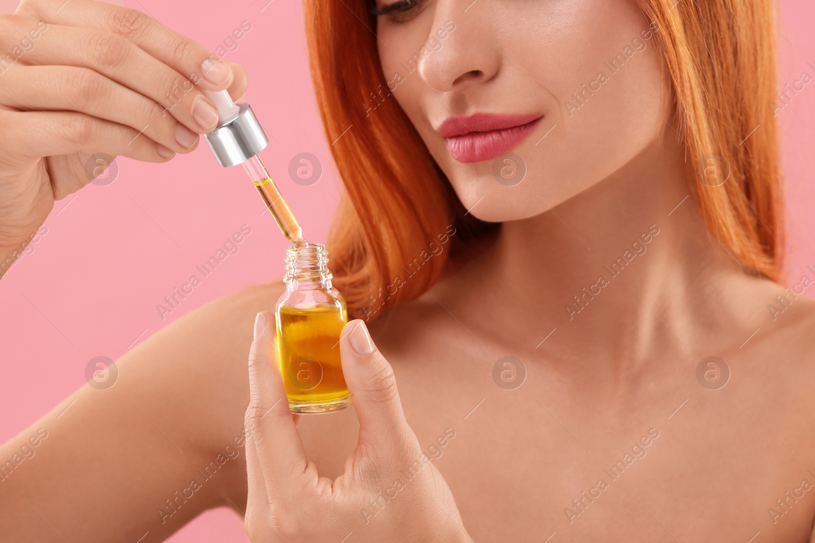 Photo of Beautiful young woman with bottle of cosmetic serum on pink background, closeup