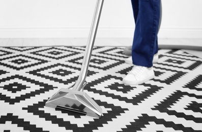 Male worker removing dirt from carpet with professional vacuum cleaner indoors