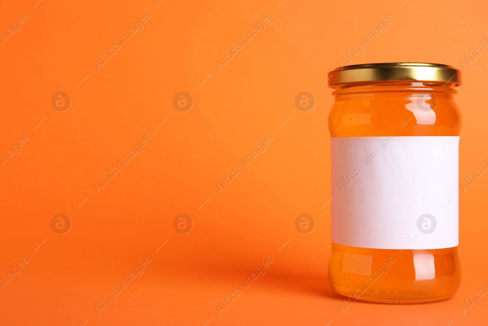Photo of Jar of organic honey with blank label on orange background. Space for text
