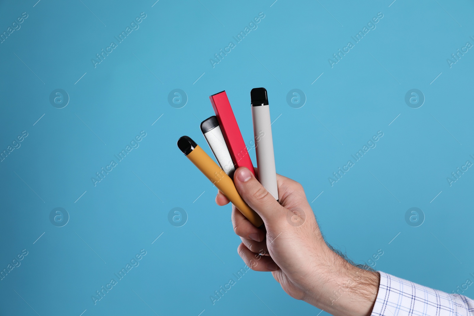 Photo of Man holding electronic cigarettes on light blue background, closeup