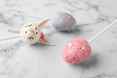 Photo of Delicious sweet cake pops for Easter celebration on white marble table, closeup