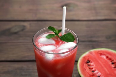 Photo of Glass of delicious watermelon drink with mint, ice cubes and fresh cut fruit against wooden background, closeup