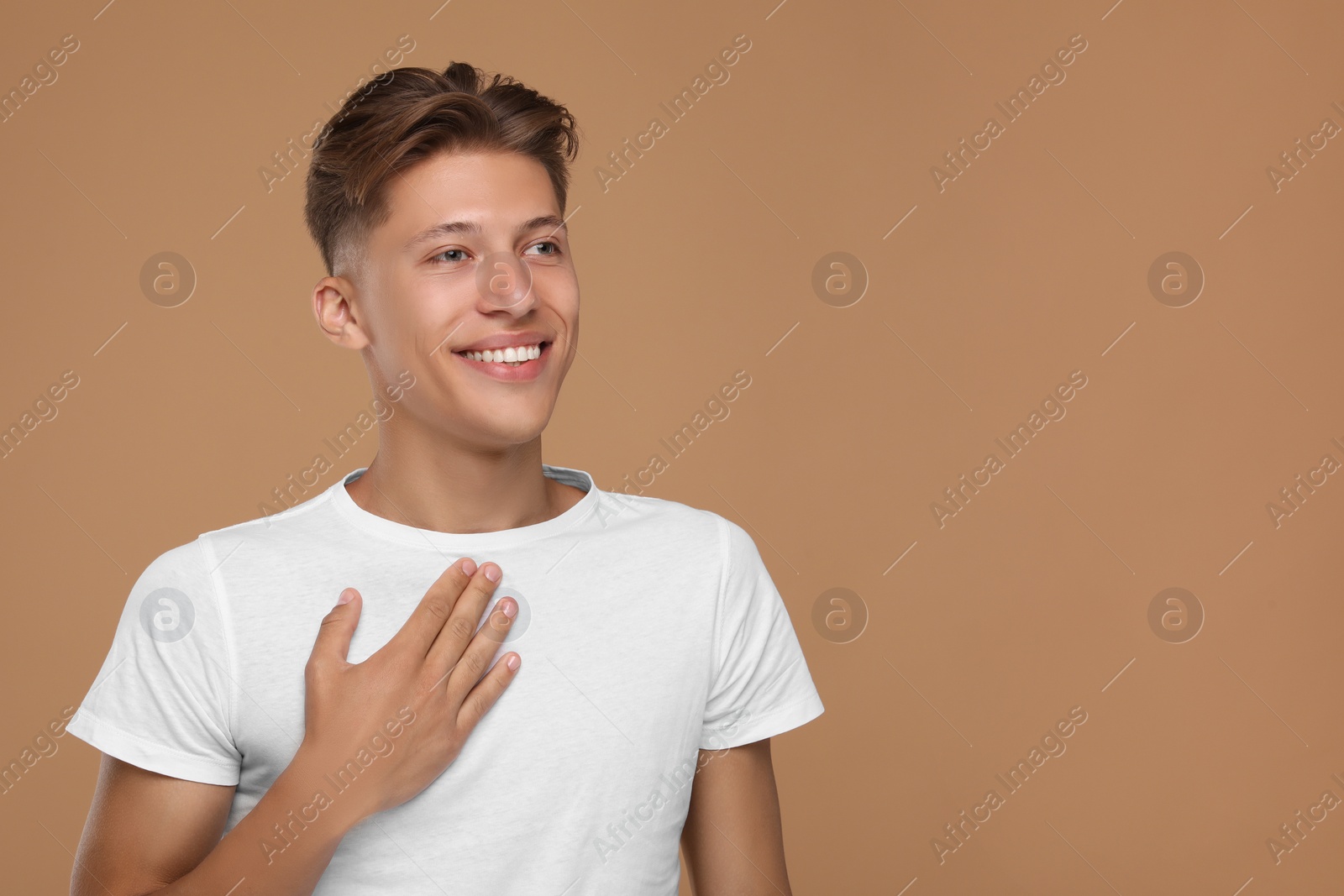 Photo of Thank you gesture. Handsome grateful man with hand on chest against brown background, space for text