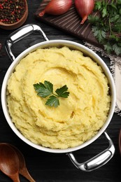Pot of tasty mashed potatoes with parsley on black wooden table, flat lay