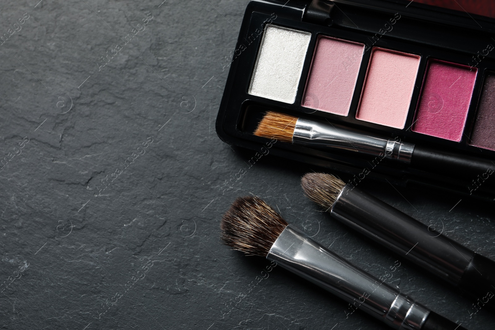 Photo of Beautiful eye shadow palette and brushes on dark grey textured table, flat lay. Space for text