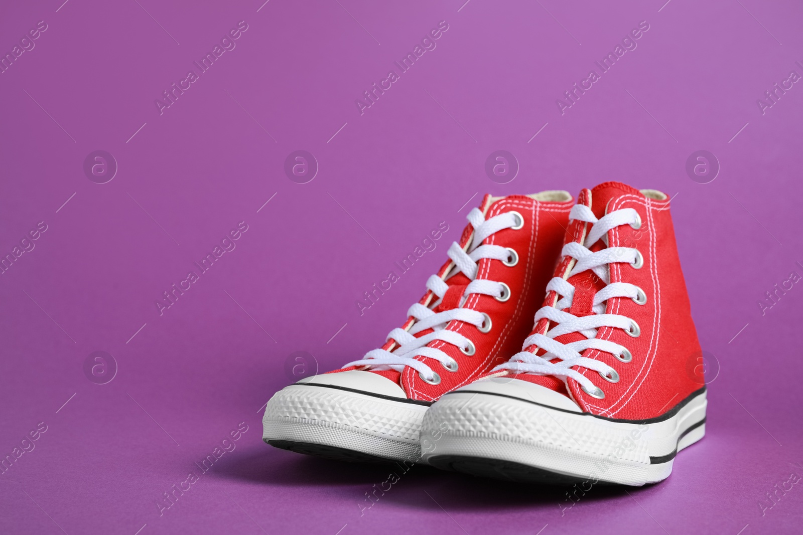 Photo of Pair of new stylish red sneakers on purple background. Space for text