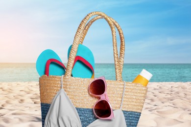 Image of Stylish bag and other beach accessories on sand near sea