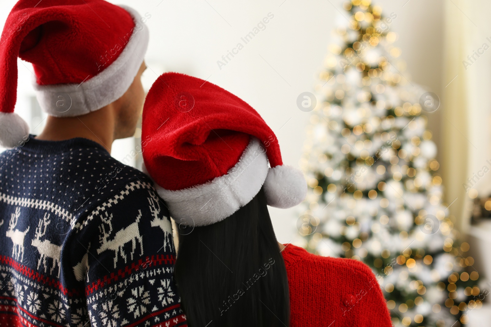 Photo of Couple in Santa hats at home, back view. Christmas celebration