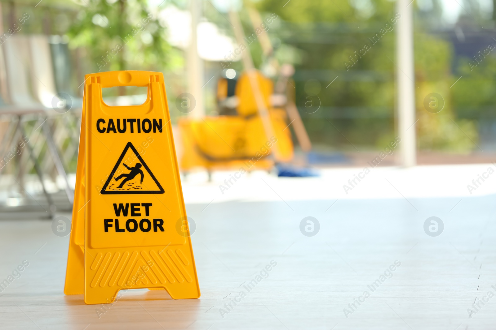 Photo of Safety sign with phrase Caution wet floor and blurred mop bucket on background. Cleaning service