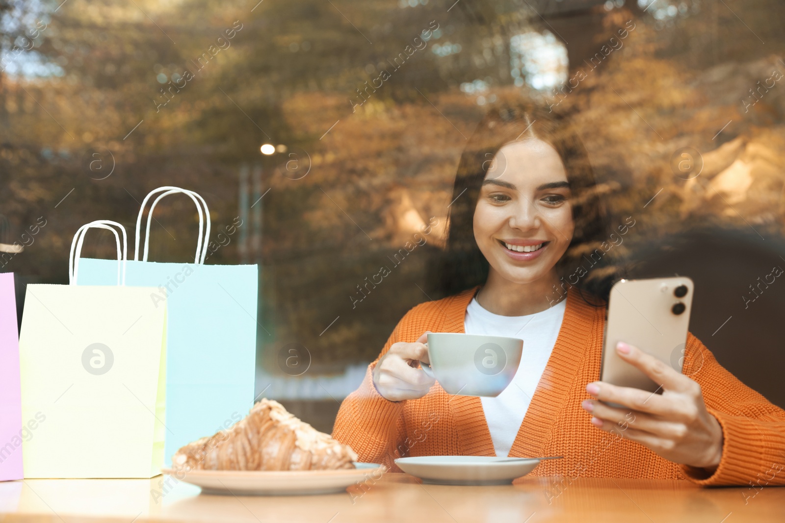 Photo of Special Promotion. Happy young woman with cup of drink using smartphone in cafe, view from outdoors