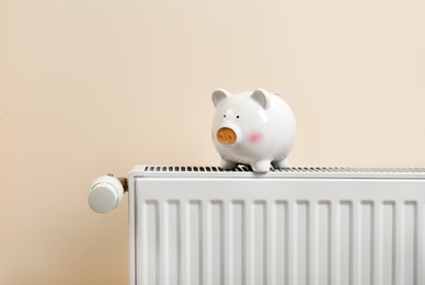 Piggy bank on heating radiator against light background