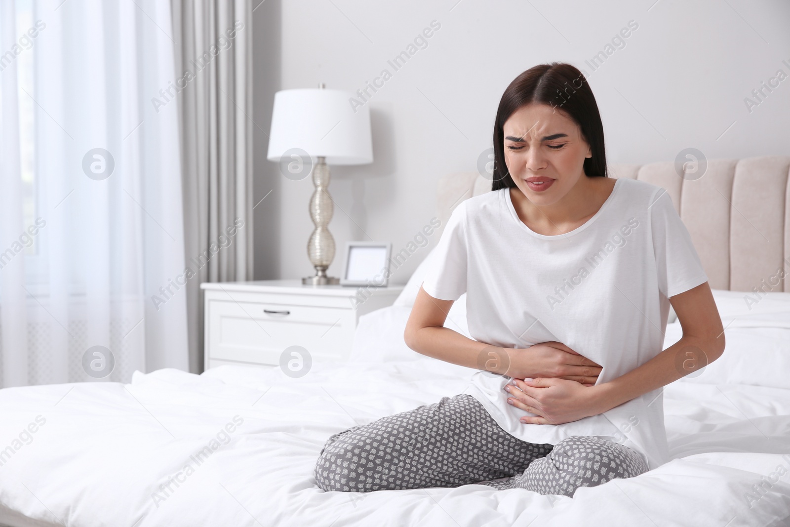 Photo of Young woman suffering from stomach ache in bedroom