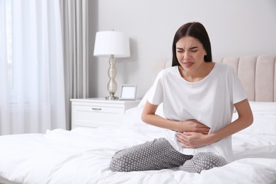 Photo of Young woman suffering from stomach ache in bedroom