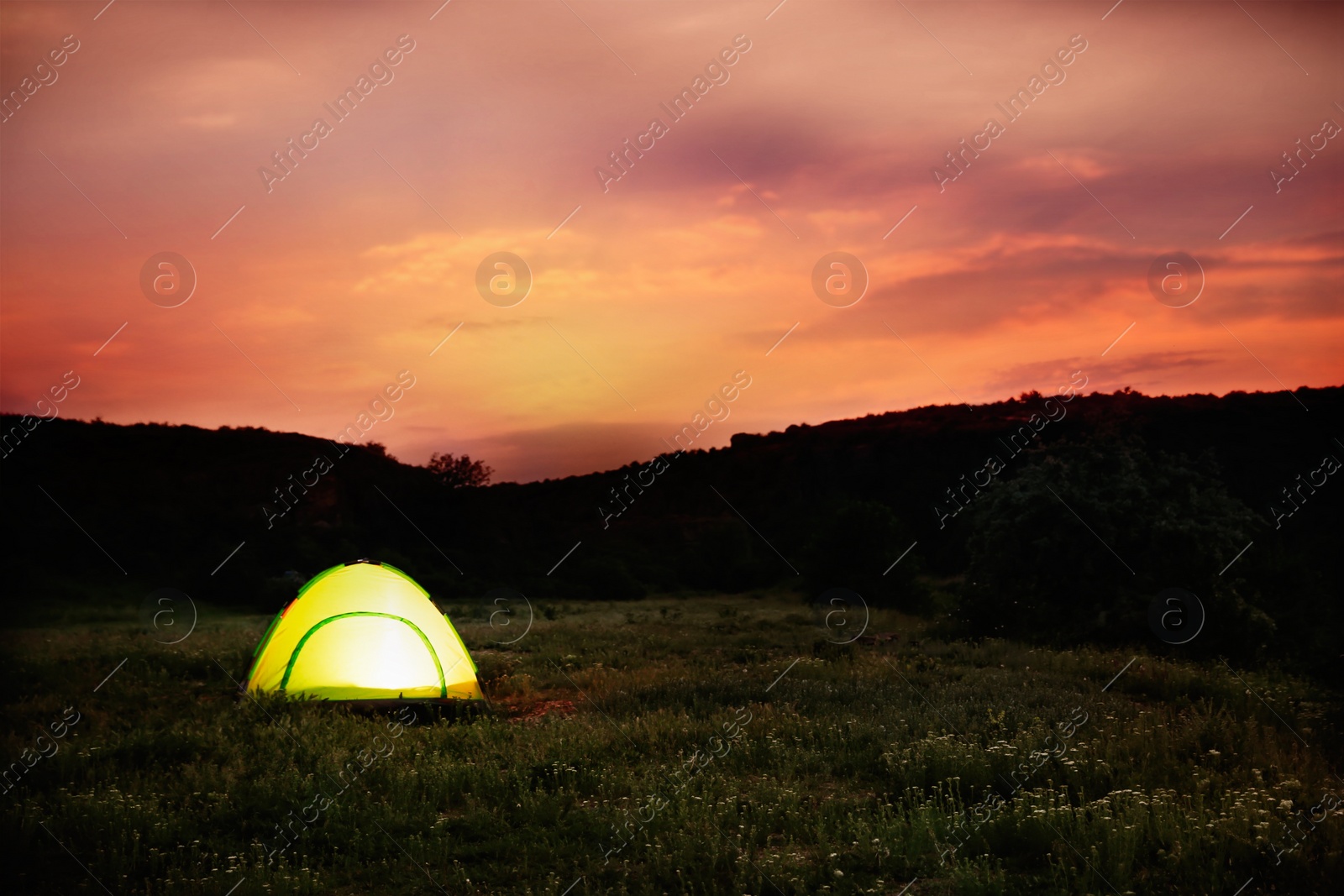 Image of Small camping tent glowing in twilight, outdoors