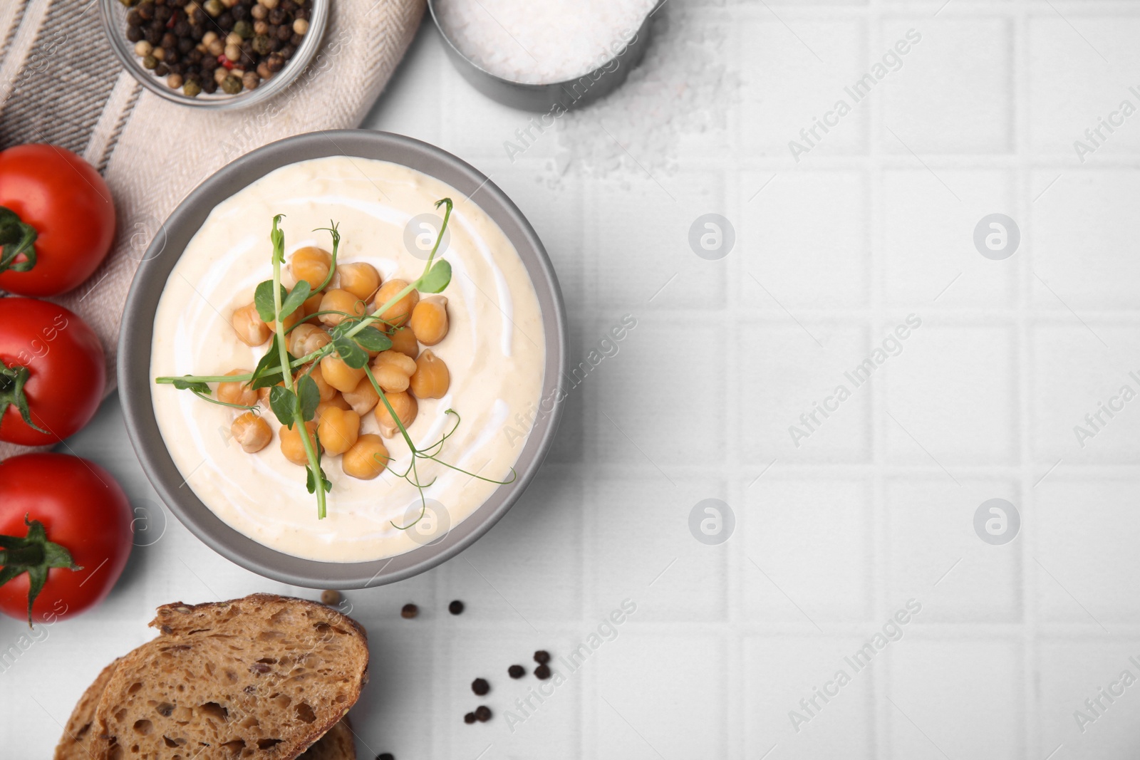 Photo of Flat lay composition of tasty chickpea soup in bowl on white tiled table. Space for text