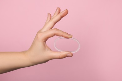 Photo of Woman holding diaphragm vaginal contraceptive ring on pink background, closeup. Space for text