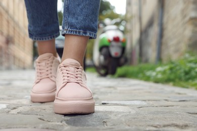 Photo of Woman in stylish sneakers walking on city street, closeup. Space for text