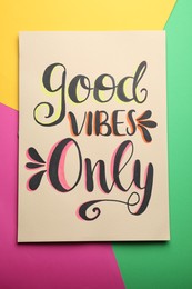 Photo of Card with life-affirming phrase Good Vibes Only on colorful background, top view