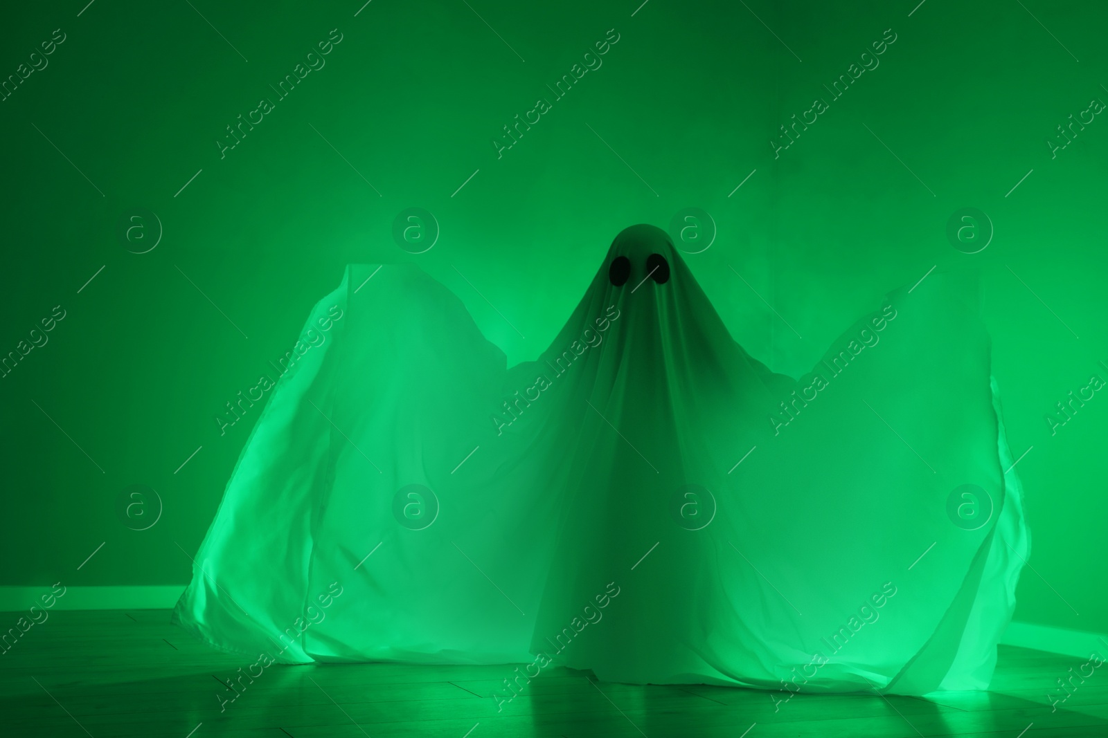 Photo of Creepy ghost. Woman covered with sheet in green light