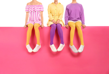 Photo of Group of women wearing bright tights and stylish shoes sitting on color background, closeup