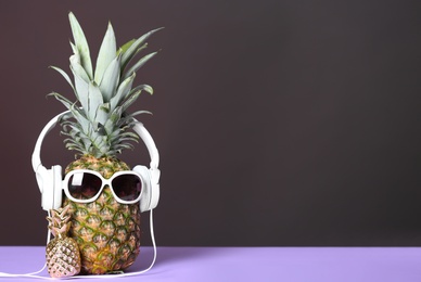 Photo of Pineapple with headphones and sunglasses on table against dark background. Space for text
