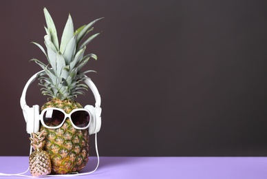 Pineapple with headphones and sunglasses on table against dark background. Space for text