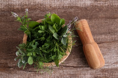 Mortar, pestle and different herbs on wooden table, top view