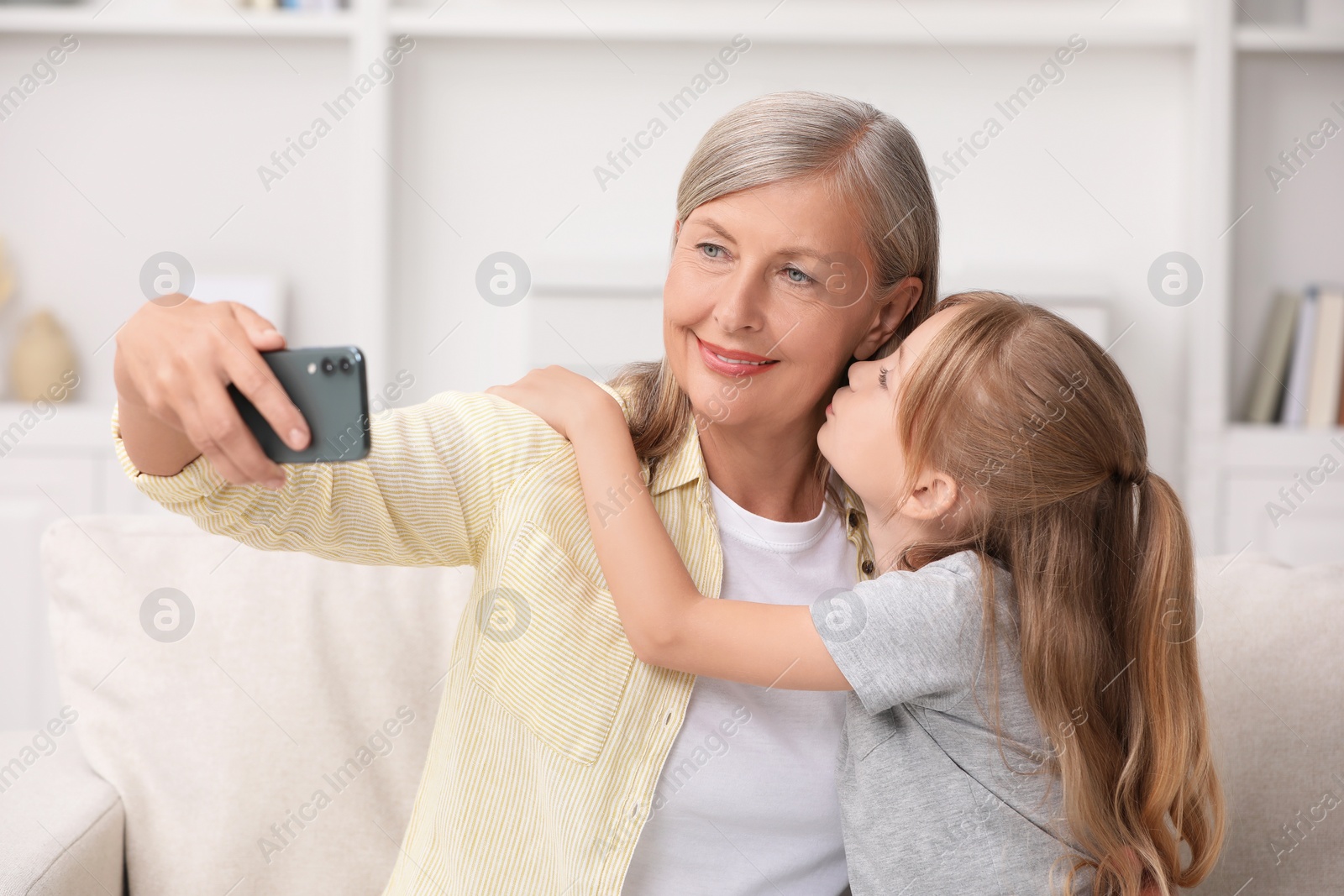 Photo of Happy grandmother taking selfie with her granddaughter at home